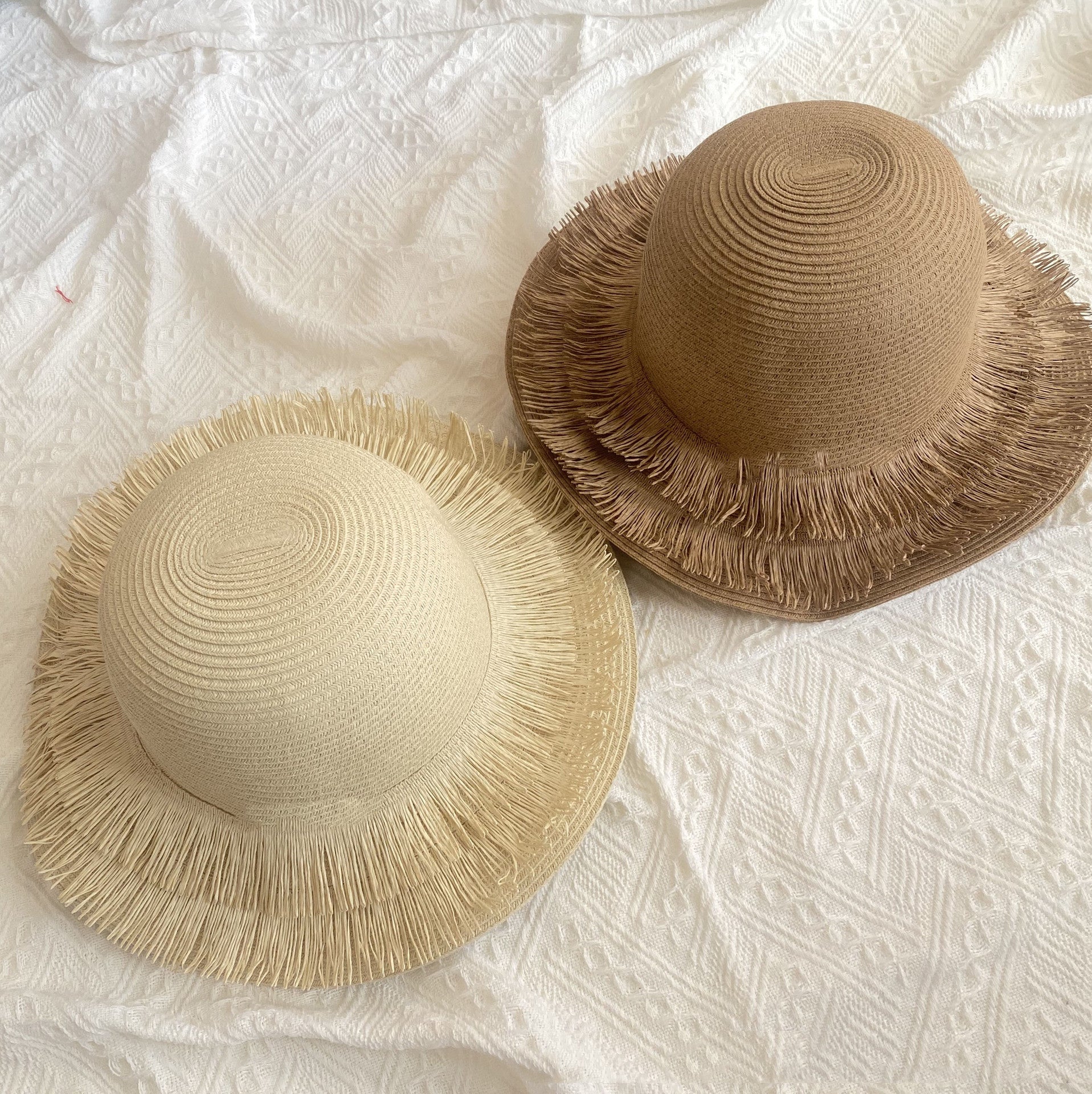 Two Fringed Designed Seaside Beach Straw Hats by Beachy Cover Ups on a white bed.