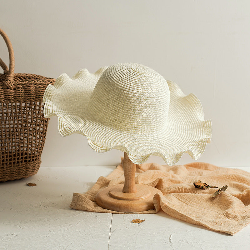 A Foldable Wavy Edge Windproof Beach Hat by Beachy Cover Ups on a wooden stand next to a wicker basket.