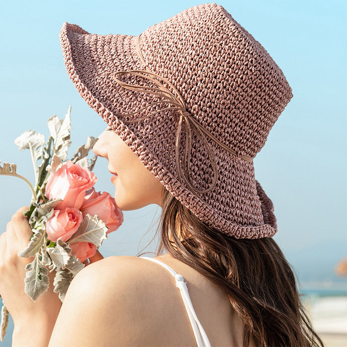 A woman wearing an Elegant Foldable Travel Beach Straw Hat by Beachy Cover Ups, with flowers on it, perfect for sun-chasing adventures.