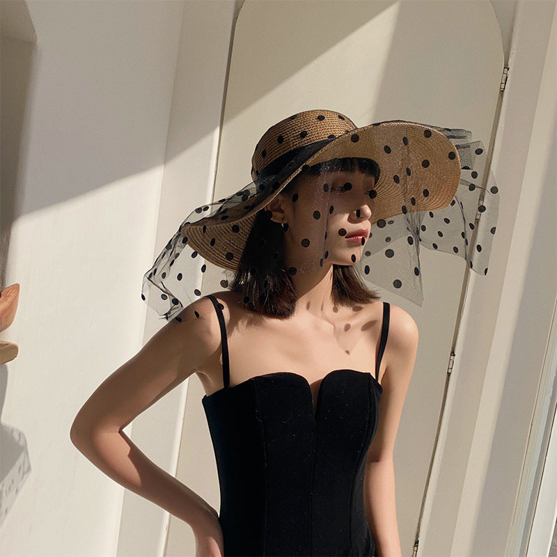 A woman wearing a black dress and a Big Brim Lace Mesh Polka Dot Beach Hat by Beachy Cover Ups for sun protection.