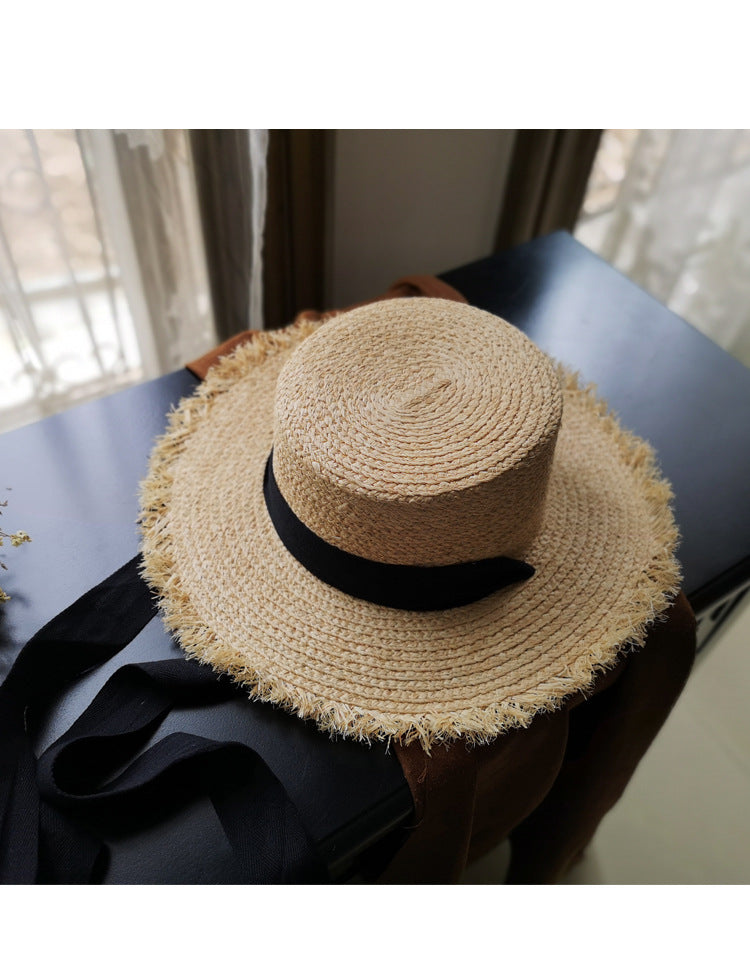 A Fringed Edge Straw Bowknot Sun Hat by Beachy Cover Ups sits on a table next to a window.