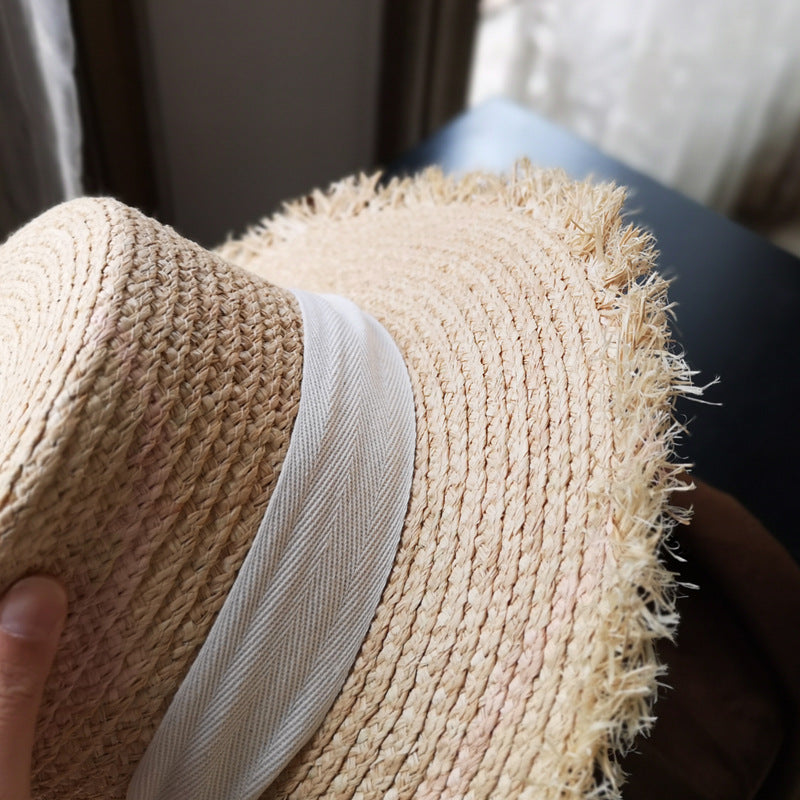 A person is holding a Fringed Edge Straw Bowknot Sun Hat by Beachy Cover Ups in front of a window.