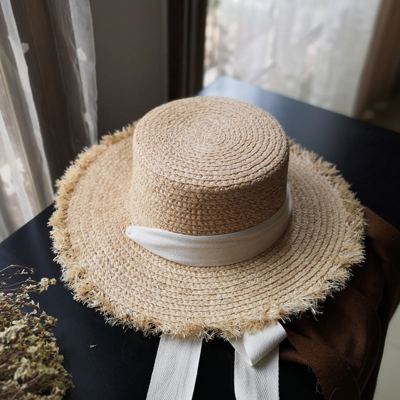 A Fringed Edge Straw Bowknot Sun Hat by Beachy Cover Ups sitting on top of a table.