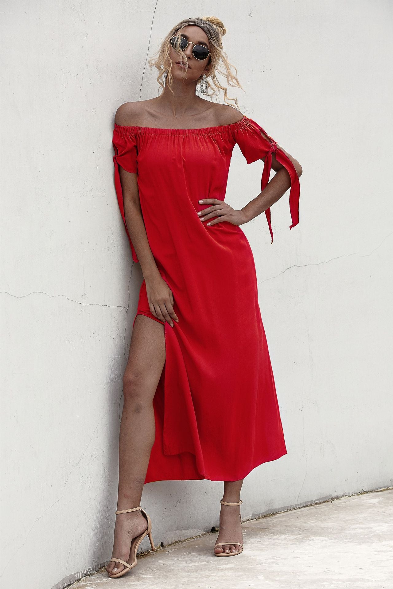 A woman in a Summer Straight Shoulder Split Beach Dress from Beachy Cover Ups, leaning against a wall.