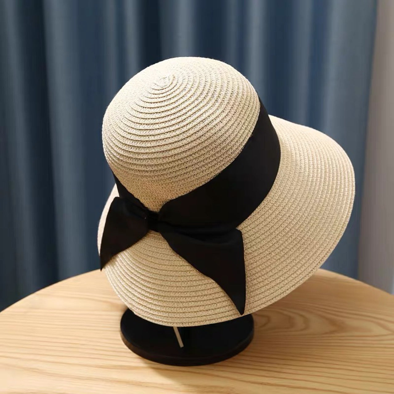 A Straw Hat Foldable Beach Sunshade with a black bow on top by Beachy Cover Ups.