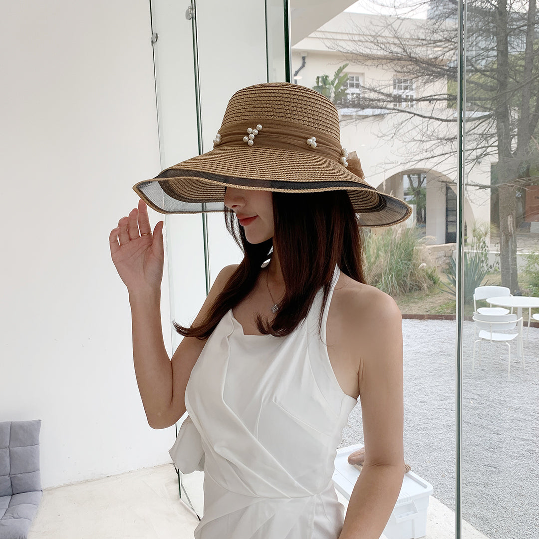 A woman wearing a white dress and a Big Brim Straw Beach Hat With Bow and Pearls from Beachy Cover Ups.