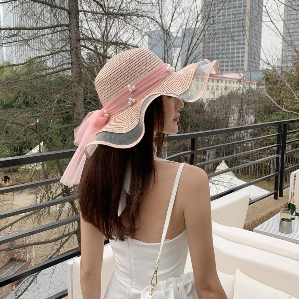 A woman wearing a Big Brim Straw Beach Hat With Bow and Pearls from Beachy Cover Ups on a balcony.