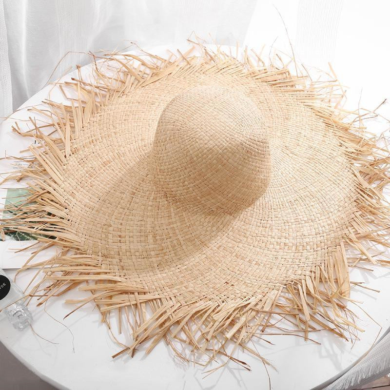 A Rustic Fringe Temperament Beach Hat by Beachy Cover Ups on top of a white table.