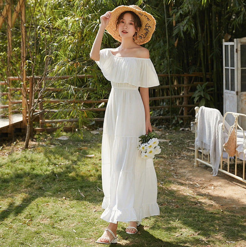 A woman in a white One-shoulder Beach Umbrella Dress by Beachy Cover Ups and a straw hat exuding coastal elegance.