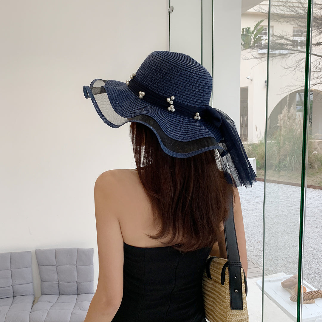 A woman wearing a blue Big Brim Straw Beach Hat With Bow and Pearls by Beachy Cover Ups and black dress.