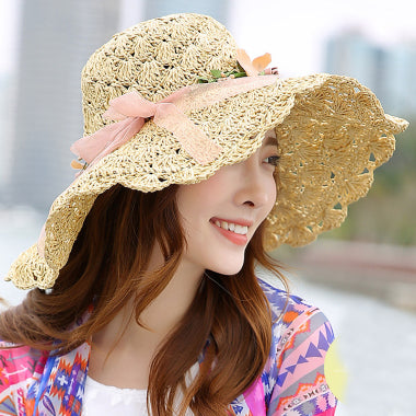 A young woman wearing a Floral Foldable Big Brim Beach Straw Hat by Beachy Cover Ups for sun protection at the beach.