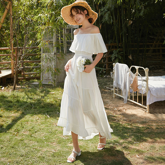 A woman wearing a white One-shoulder Beach Umbrella Dress by Beachy Cover Ups exudes coastal elegance.