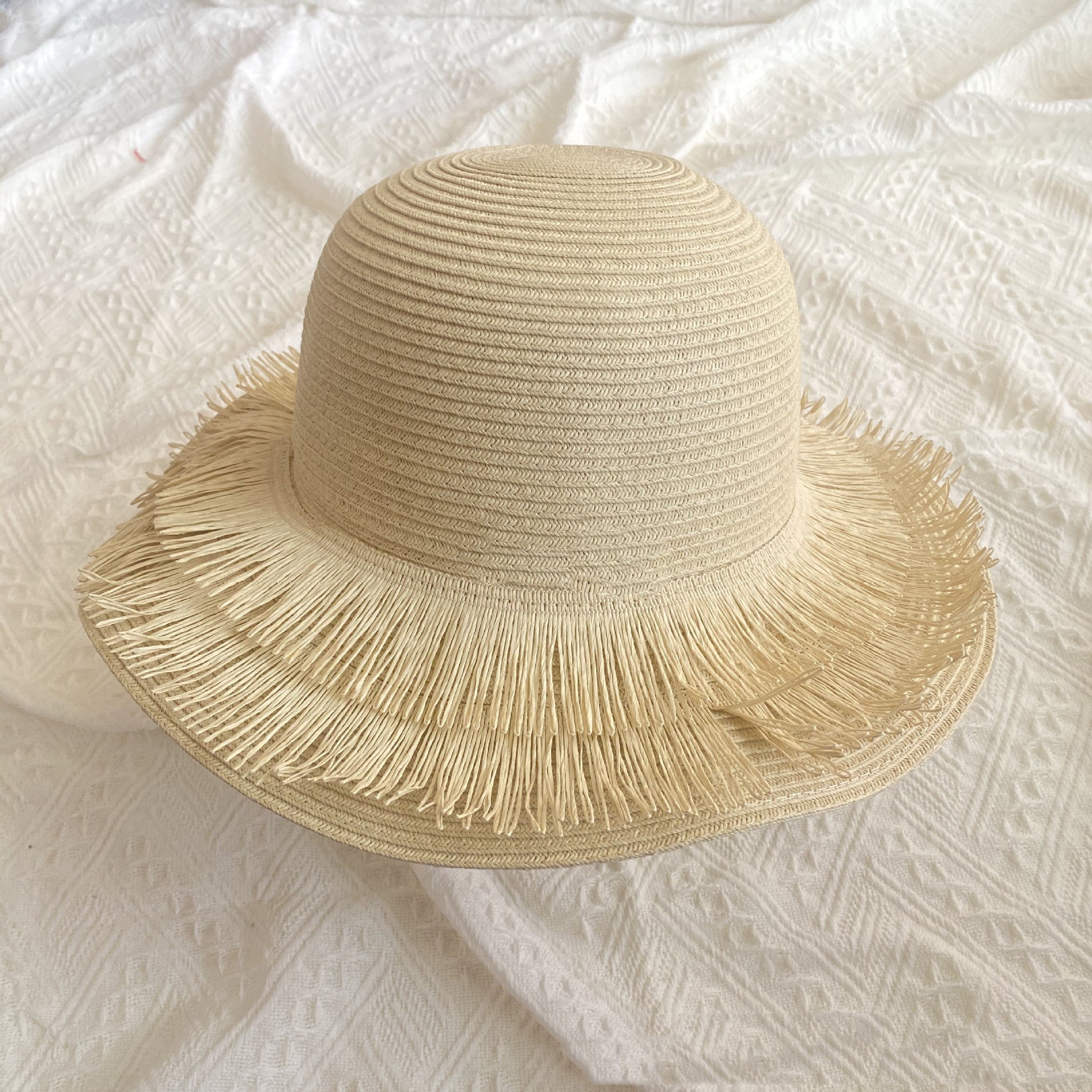 A Fringed Designed Seaside Beach Straw Hat with floral finesse on top of a white bed by Beachy Cover Ups.