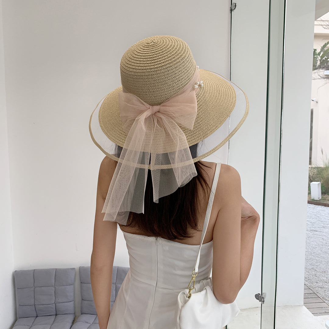 A woman wearing a Big Brim Straw Beach Hat With Bow and Pearls by Beachy Cover Ups.