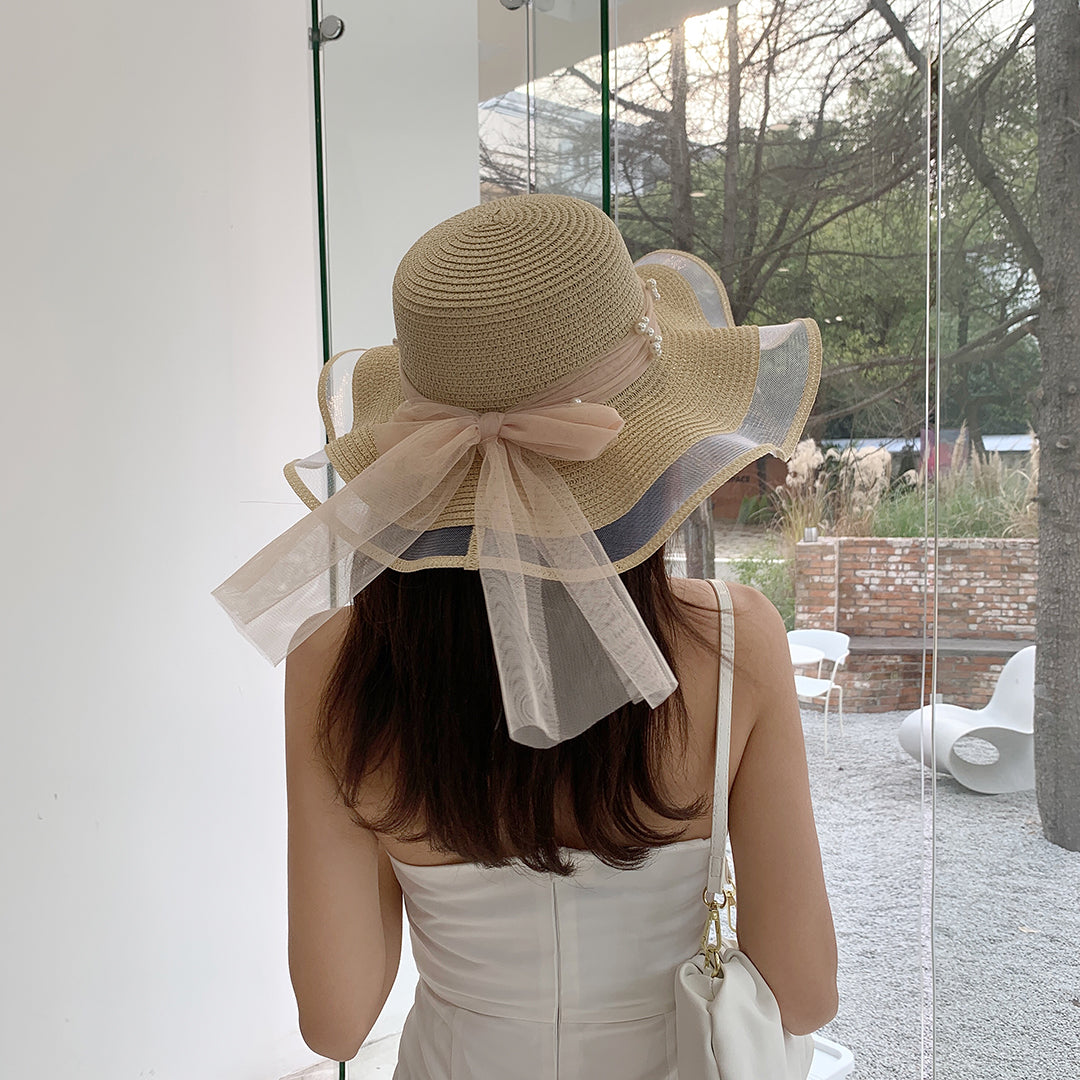 A woman wearing a Big Brim Straw Beach Hat With Bow and Pearls by Beachy Cover Ups.