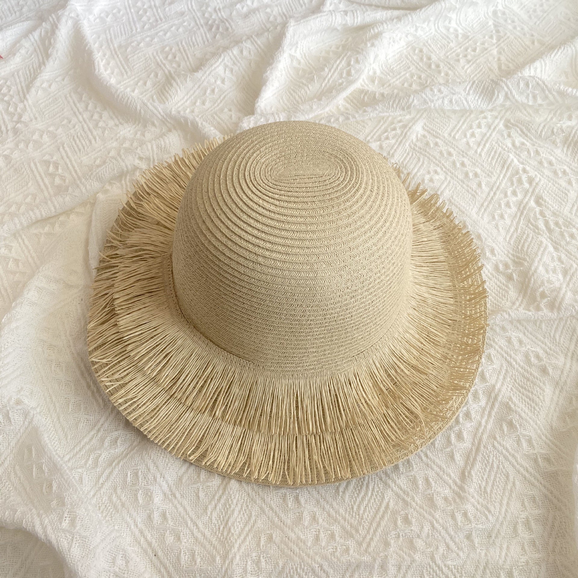A Fringed Designed Seaside Beach Straw Hat by Beachy Cover Ups providing sun protection on a white bed.