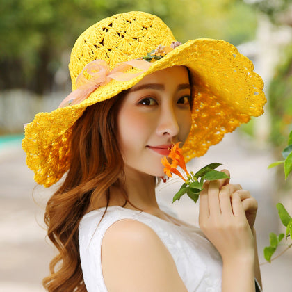 A young woman in a Floral Foldable Big Brim Beach Straw Hat by Beachy Cover Ups, holding a flower.