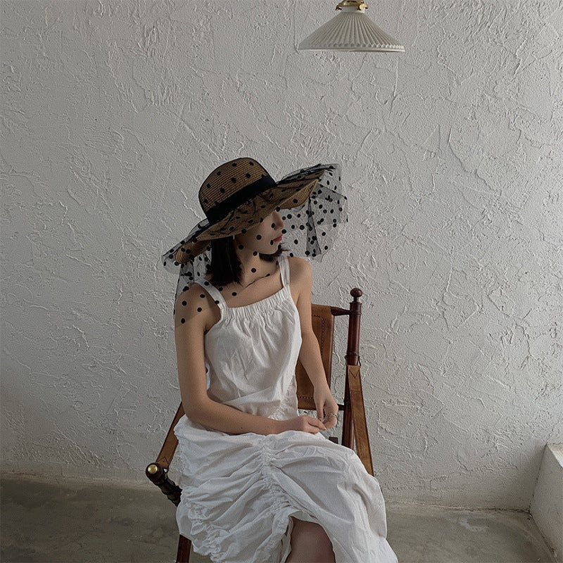 A woman wearing a Big Brim Lace Mesh Polka Dot Beach Hat by Beachy Cover Ups sitting in a chair.