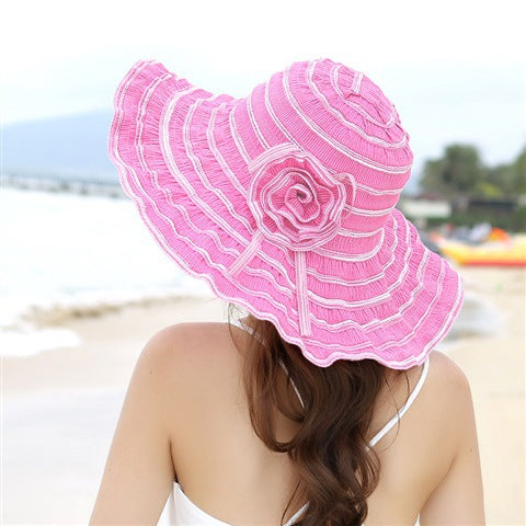 A woman wearing a Rippled Colored Flower Beach Hat from Beachy Cover Ups on the beach.