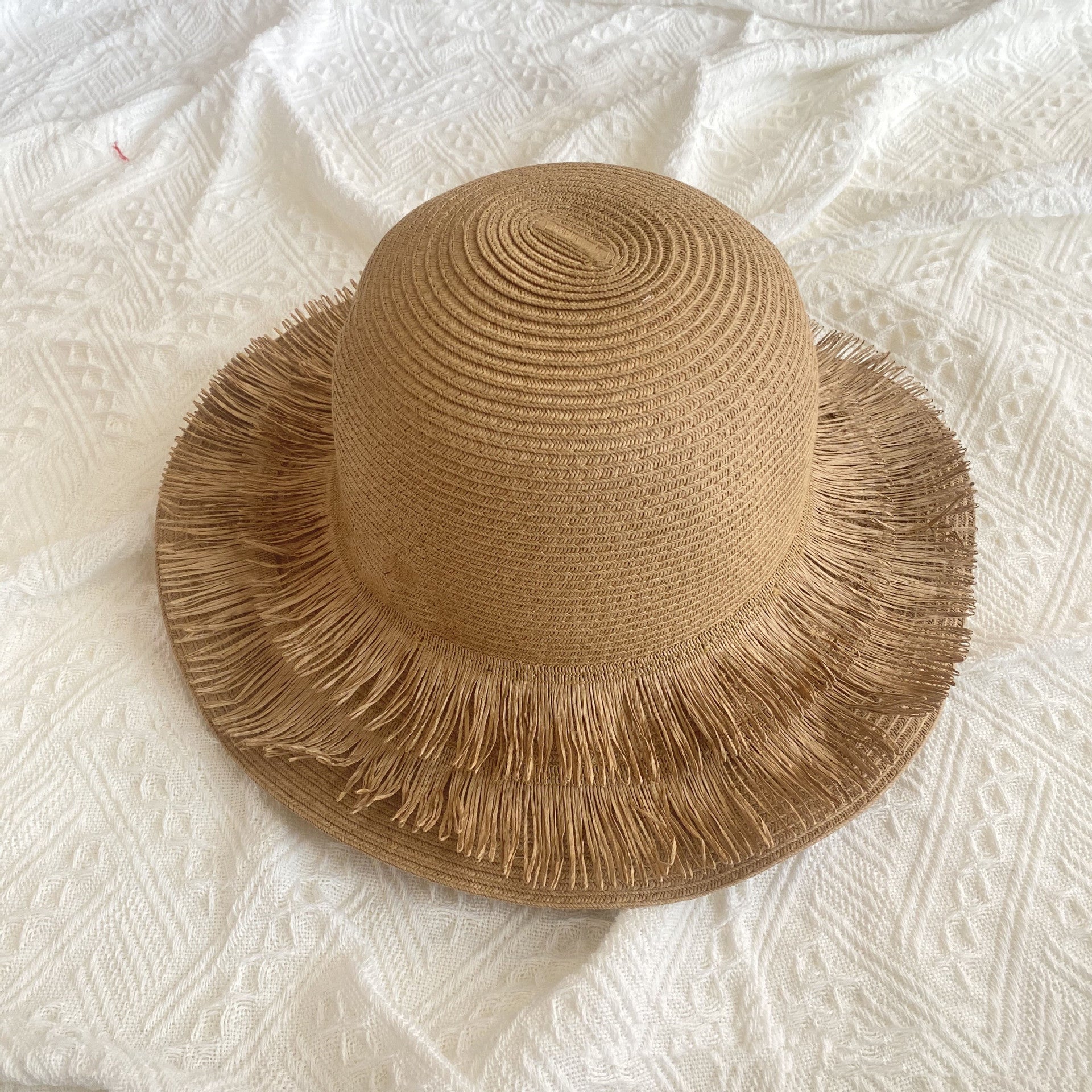 A Fringed Designed Seaside Beach Straw Hat by Beachy Cover Ups on top of a white bed.