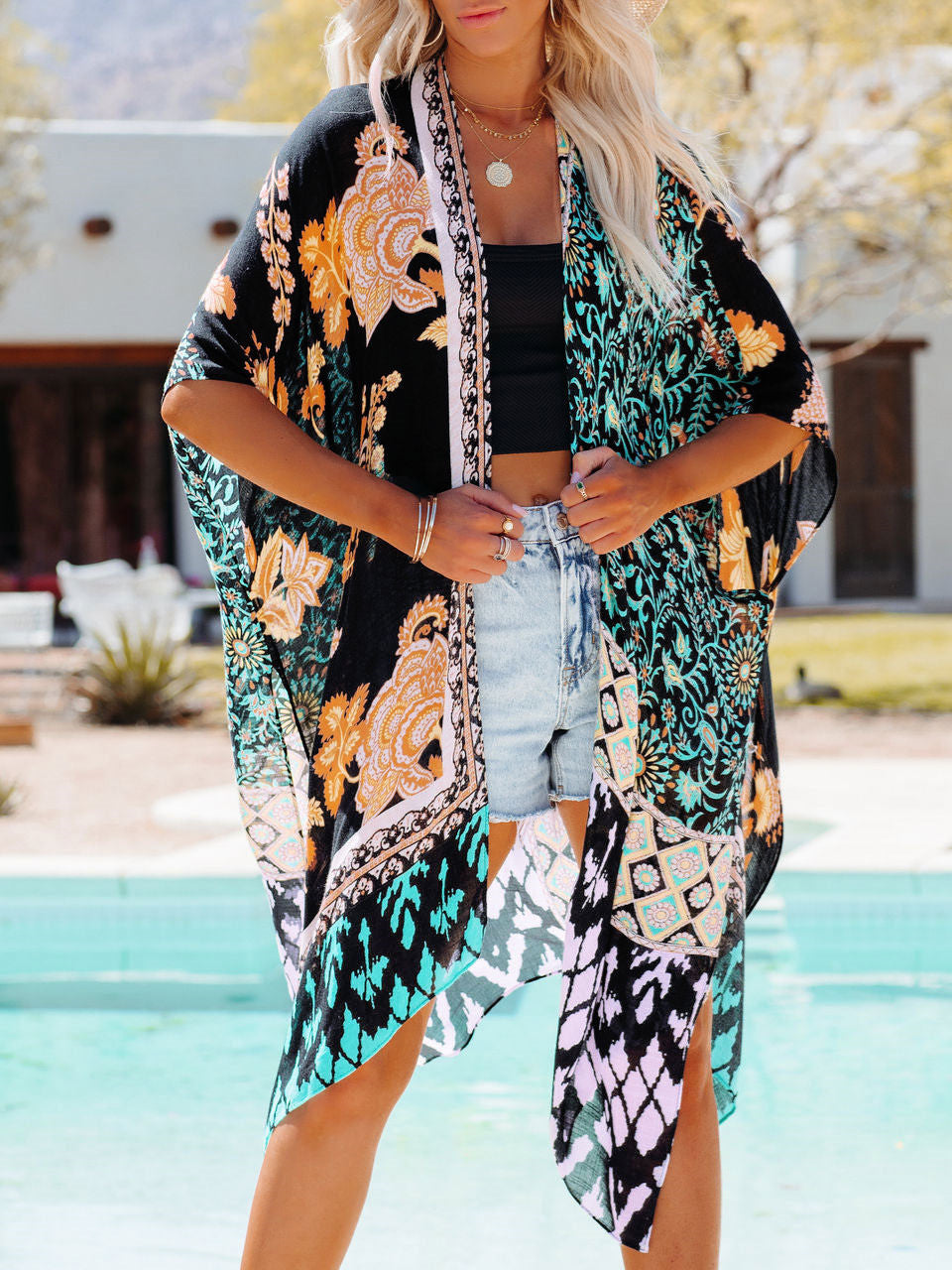 A woman wearing a vibrant printed Tropical Beach Cardigan Cover Up by Beachy Cover Ups by a pool.