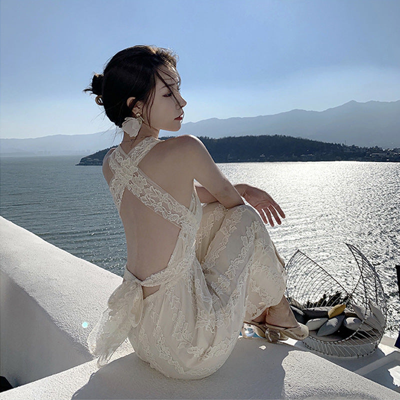 A woman in a High Waist Open Back Floral Apricot Beach Dress from Beachy Cover Ups sitting on a ledge.