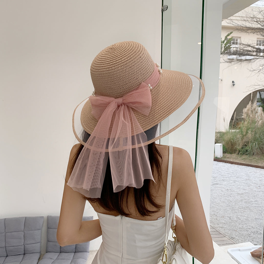 A woman wearing a Big Brim Straw Beach Hat With Bow and Pearls by Beachy Cover Ups and white dress.