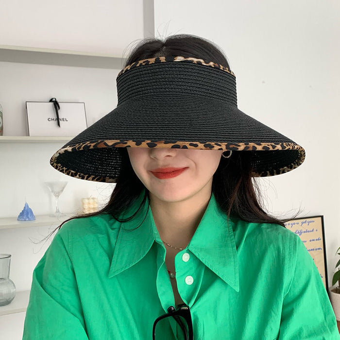 A woman wearing a black Big Brim Cheetah Print Edge Straw Visor by Beachy Cover Ups and green shirt.