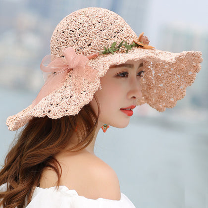 A woman in a Floral Foldable Big Brim Beach Straw Hat by Beachy Cover Ups is posing by the water for sun protection.