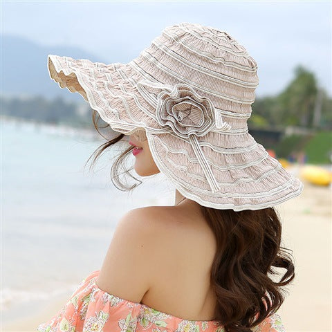 A woman wearing a Rippled Colored Flower Beach Hat by Beachy Cover Ups on the sandy summer shore.