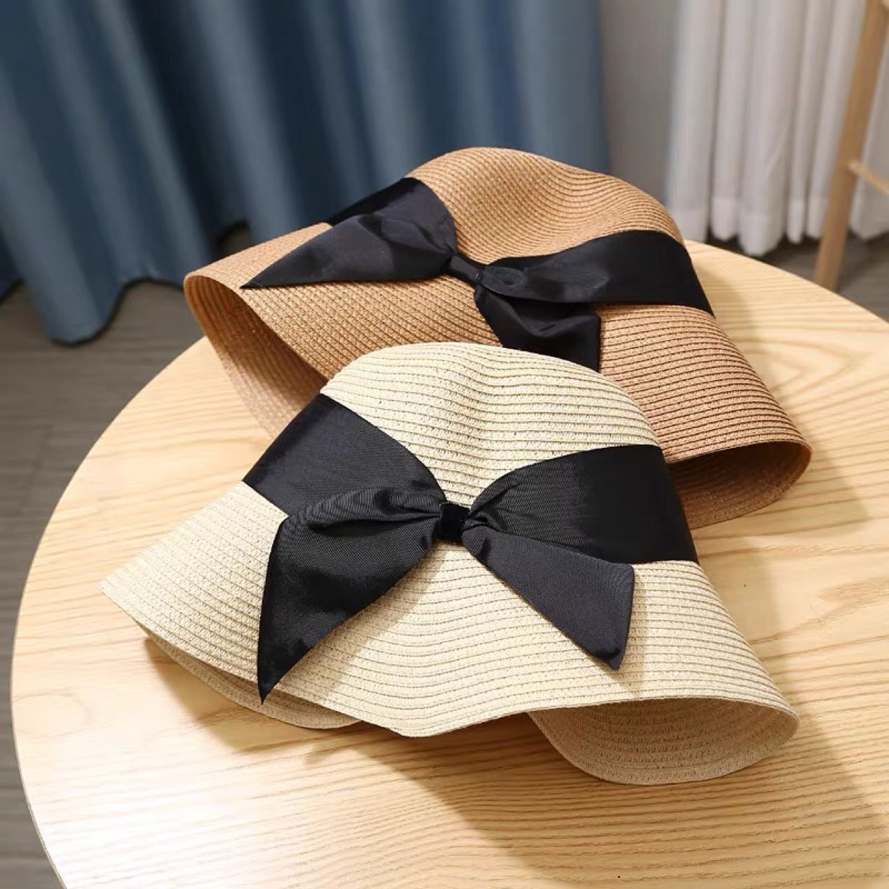 Two Beachy Cover Ups Straw Hat Foldable Beach Sunshades with black bows on top of a table.