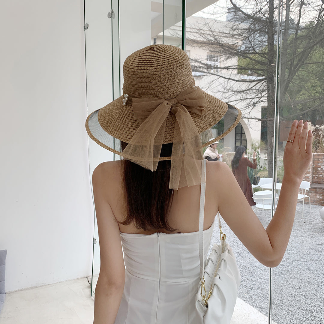 A woman wearing a Big Brim Straw Beach Hat With Bow and Pearls by Beachy Cover Ups and a white dress.